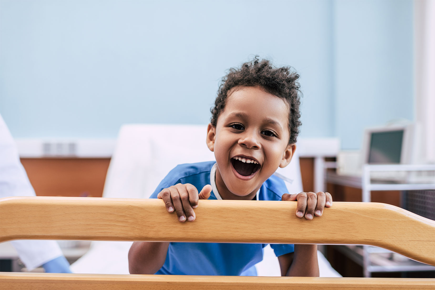 child smiling at edge of hospital bed in room with light blue walls